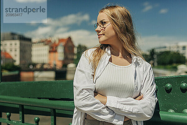 Stylish young woman with arms crossed standing on bridge