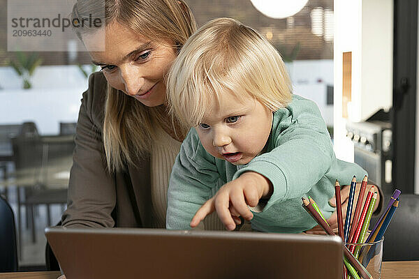 Blond boy reaching at tablet PC with freelancer mother at home