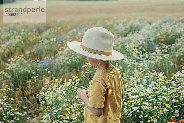 Young boy wearing shirt and hat standing in meadow