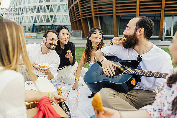 Happy friends together having snacks and enjoying picnic in park