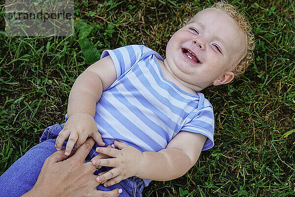 Mother tickling her laughing son on the grass.