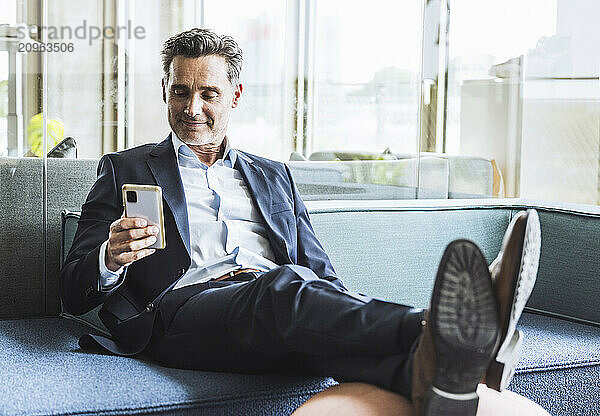 Smiling mature businessman using smart phone on sofa in office