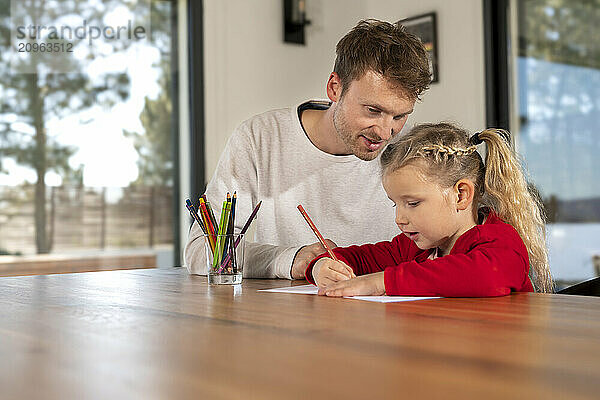 Blond girl drawing on paper sitting with father at home