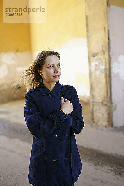 Thoughtful woman wrapped in jacket standing on road in alley