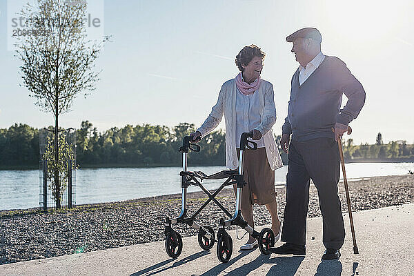 Happy senior couple walking together near river on sunny day