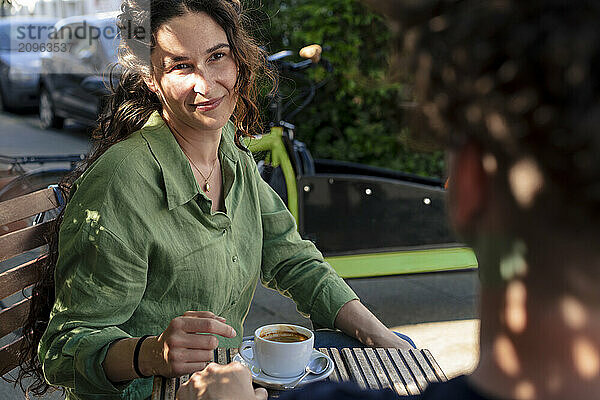 Smiling woman sitting near table with coffee cup at street