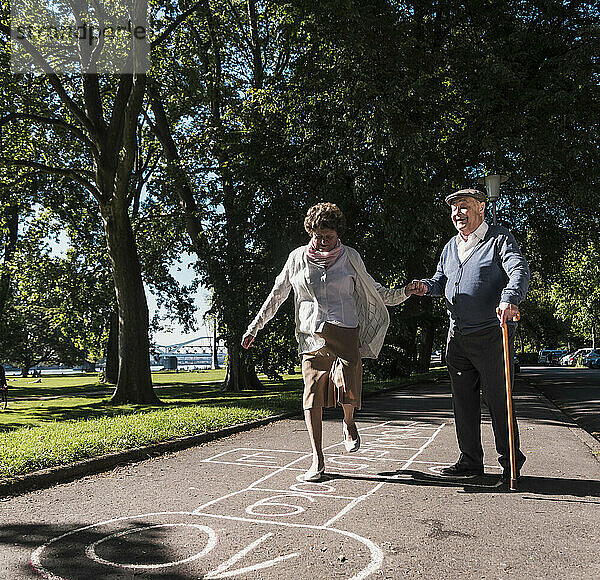 Happy man holding hands with senior woman playing hopscotch in park