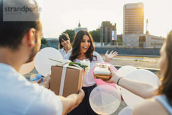 Surprised woman with friends giving gifts and celebrating birthday together