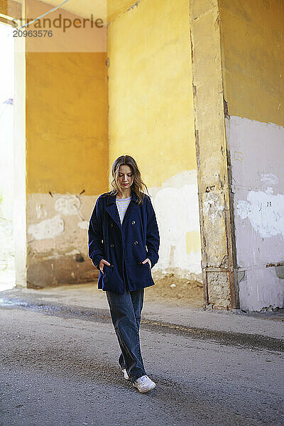 Woman with hands in pockets standing on road in old alley