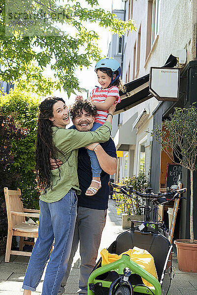 Happy man carrying daughter on shoulder and standing with woman at street