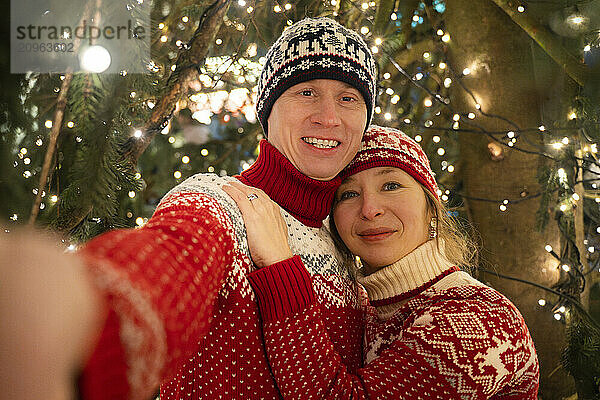 Man and beautiful woman taking selfie near christmas tree