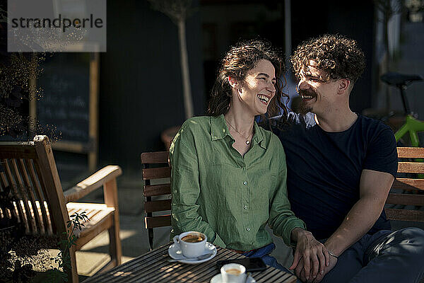 Happy couple sitting near table on bench at street