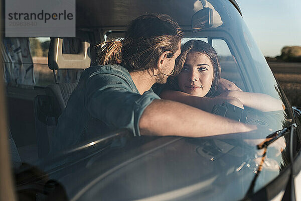 Romantic young couple leaning on dashboard of van seen through glass