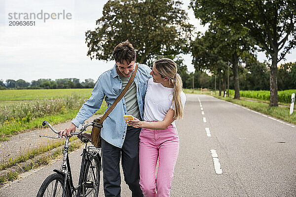 Young couple sharing smart phone and walking on road