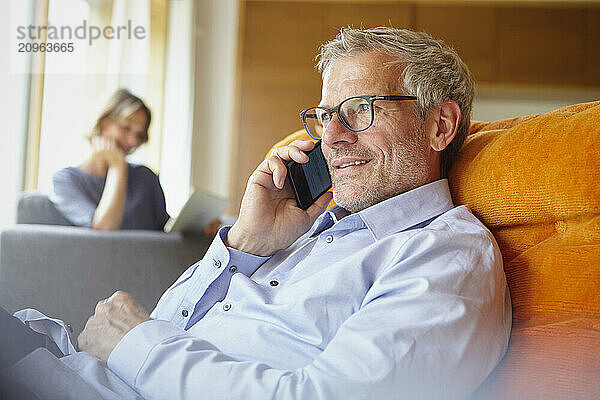 Mature man talking on smart phone and sitting on lounge chair at home