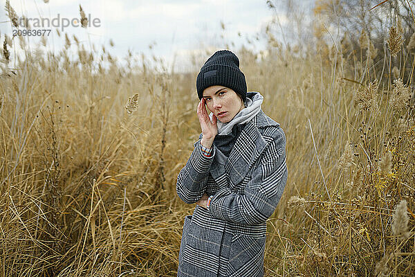 Young woman in knit hat touching head standing in reeds