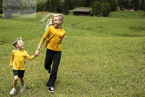 Playful sibling holding hands and running on meadow