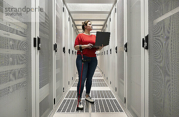 Engineer with physical disability holding laptop and working in server room at data center