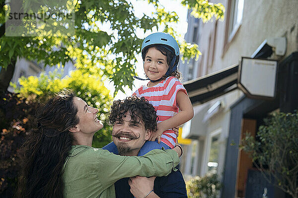 Smiling woman with man carrying daughter on shoulder at street