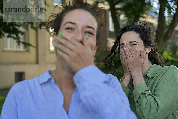 Woman with hands on mouth enjoying with friend at street