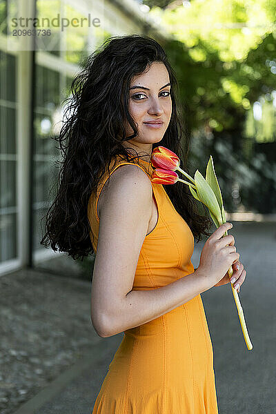 Smiling woman holding tulip flower and standing on street