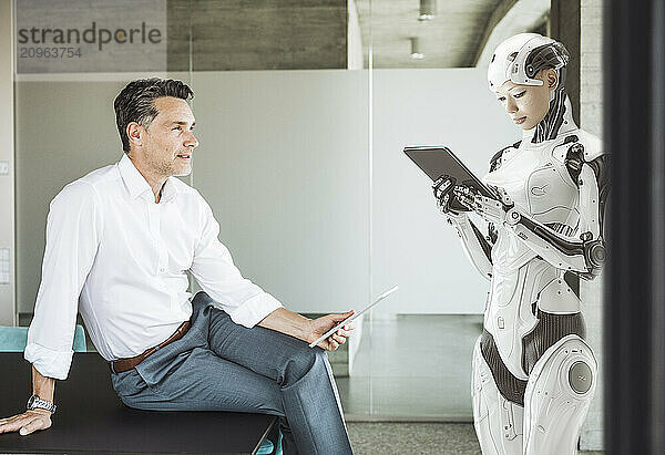 Businessman looking at cyborg using tablet PC in office