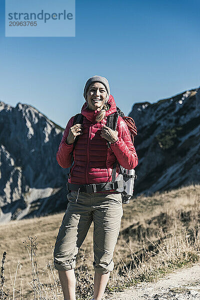 Smiling woman holding backpack and standing on mountain