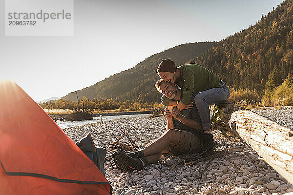 Happy woman embracing boyfriend sitting near riverside