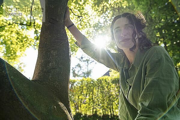 Smiling woman sitting on tree at sunny day