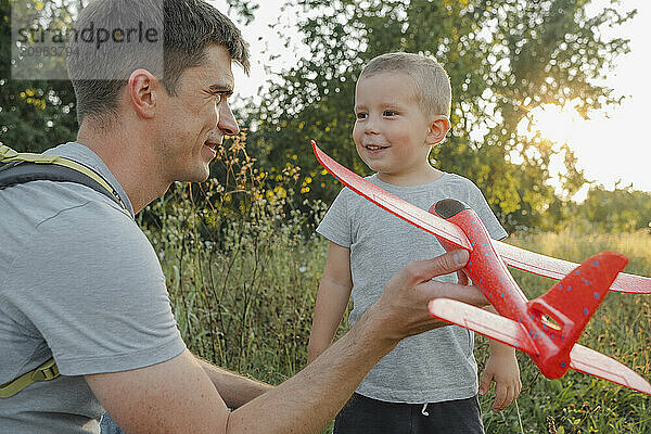 Father holding toy airplane with son standing in park