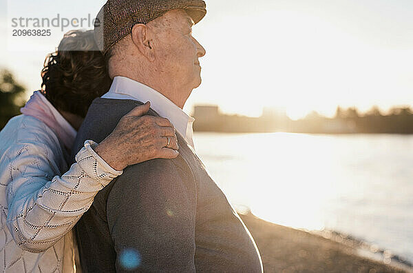 Senior woman hugging man near river at sunset