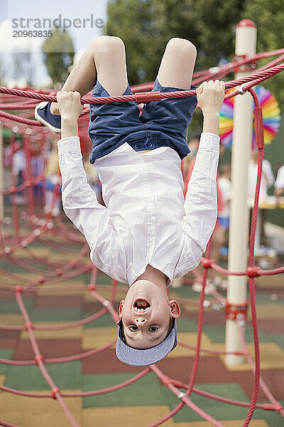 Boy hanging upside down on climbing net in playground