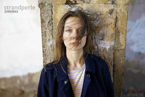 Woman with tousled hair standing near wall in abandoned house