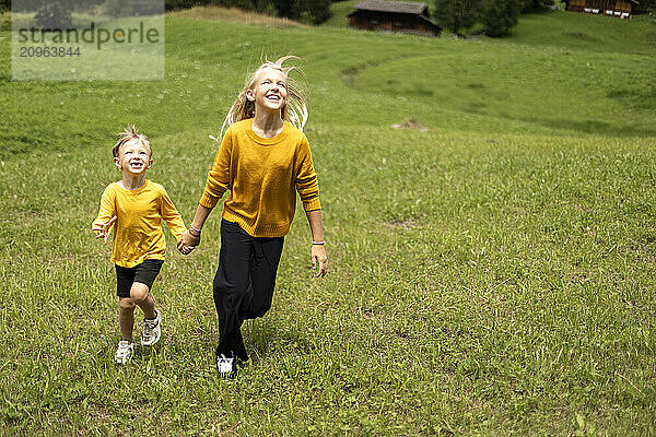 Brother and sister holding hands and running on meadow