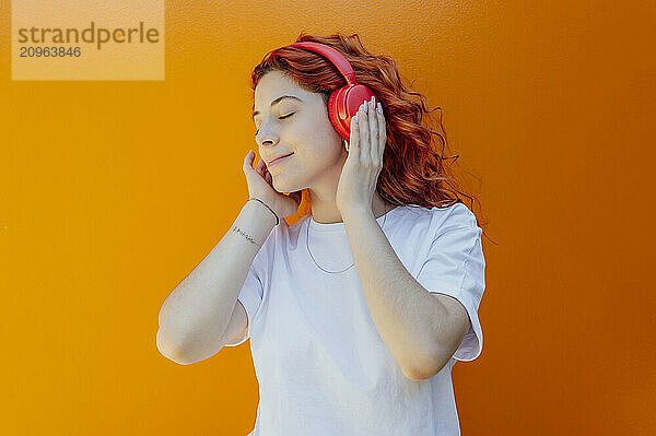 Young woman listening to music through wireless headphones against colored background