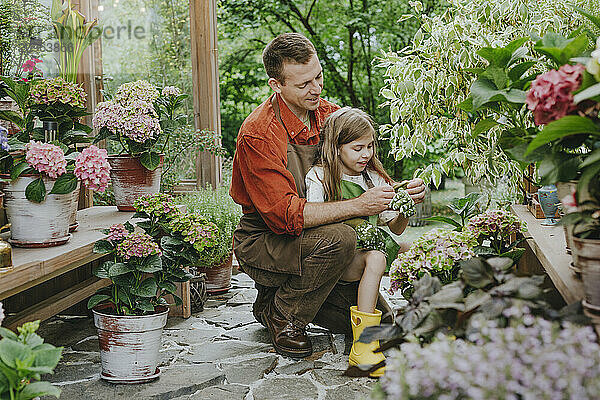 Father helping daughter in wearing gardening gloves at greenhouse