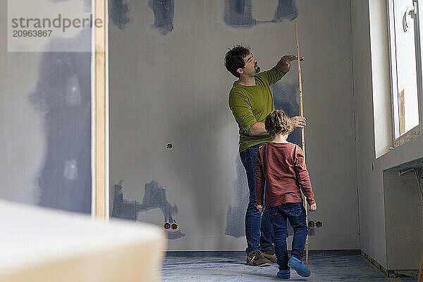 Boy near father holding measuring stick in new apartment