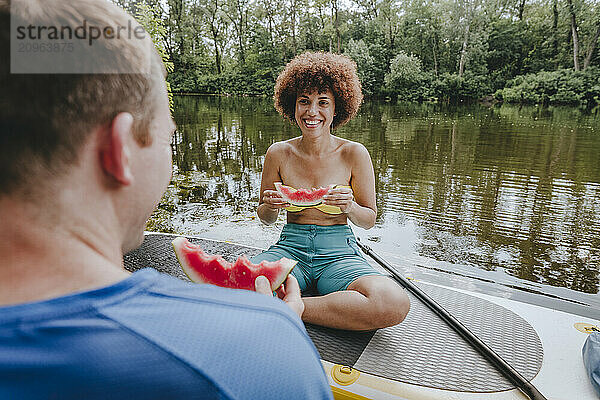 Smiling friends having watermelon on paddleboard in lake