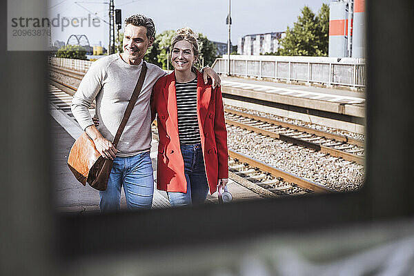 Smiling couple walking together at railroad station platform on sunny day