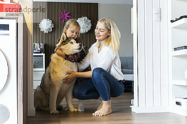 Happy mother and daughter embracing dog at home