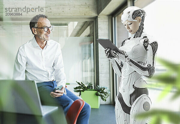 Smiling programmer looking at cyborg using tablet PC at office