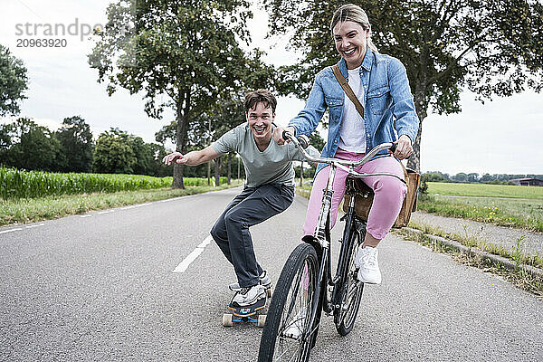 Happy woman riding bicycle with boyfriend skateboarding on road