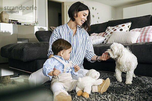 Young mother playing with dog and sitting by son in living room at home