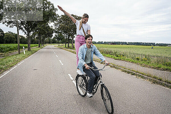 Carefree woman standing behind boyfriend riding bicycle on road