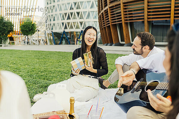 Cheerful woman holding gift boxes with friends sitting in park