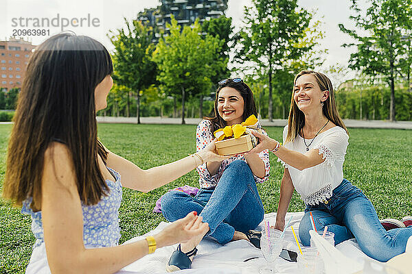 Happy woman giving gift to friends in park