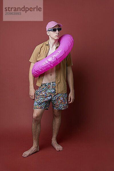 Young man with inflatable swim ring posing against brown background