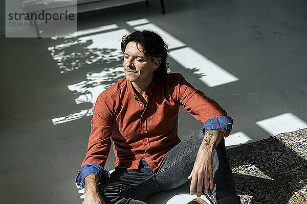 Mature man with eyes closed sitting in sunlight at home