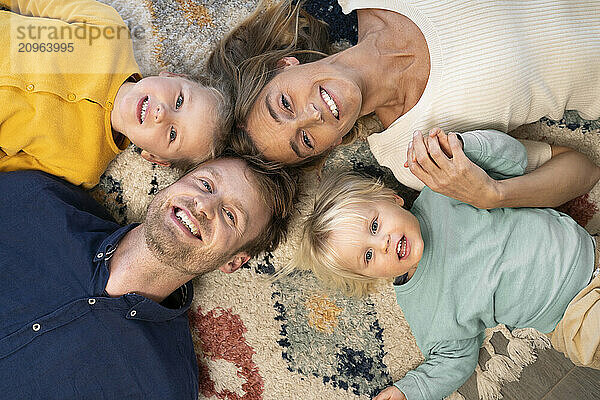 Happy man and woman with kids lying down on carpet at home