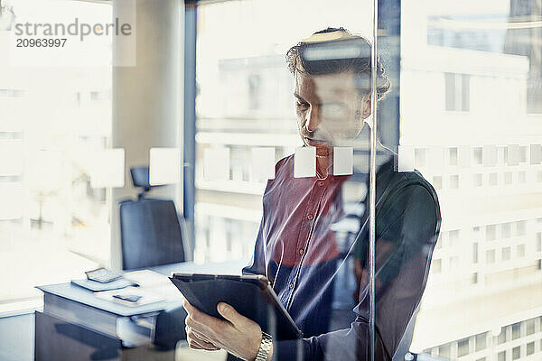 Businessman using tablet PC behind glass wall at office